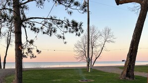 A grassy outdoor area with a wooden deck, trees, and a view of the water.
