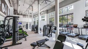 Une salle de sport spacieuse, dotée de divers appareils d’exercice, de grandes fenêtres et d’un plafond haut.