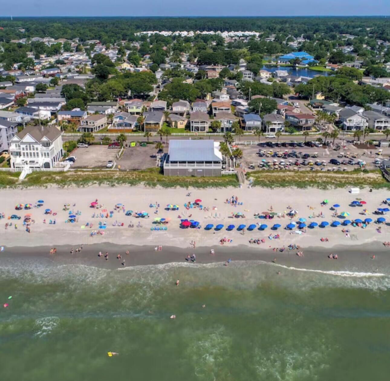 Vue aérienne d’une ville côtière avec une plage, des maisons et un parking.