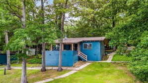 Une petite maison à un étage, à l’extérieur bleu, entourée d’arbres et bordée d’une pelouse.