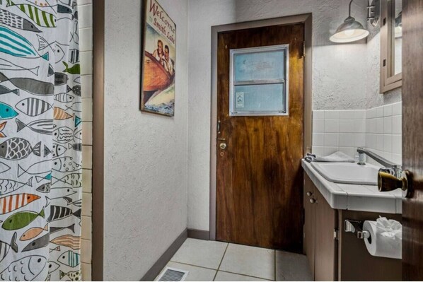 Ein Badezimmer mit Holztür, einer Duschvorhang mit Fischmuster, einem Poster an der Wand und einem Waschbecken mit Handtuch.