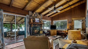 L’intérieur d’un chalet accueillant, avec une cheminée en pierre, un plafond en bois et un téléviseur.