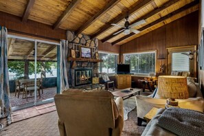 A cozy cabin interior with a stone fireplace, wooden ceiling, and a television.