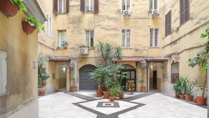 A courtyard with potted plants, a tiled floor, and a building entrance with a door and window shutters. - Charming apartment with WiFi, closed to Colosseo and Santa Maria Maggiore. (Roma)
