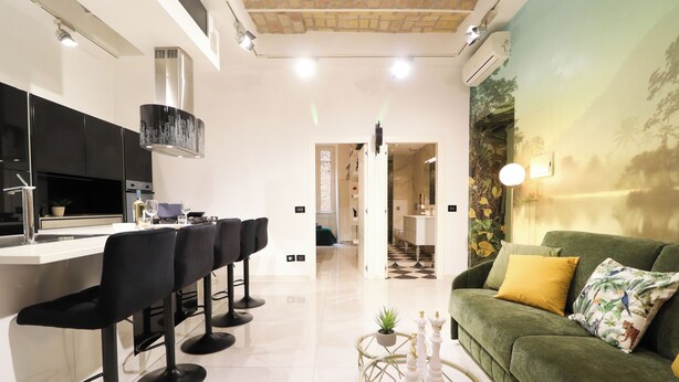 A modern kitchen with black bar stools, a green sofa, and a decorative wall mural. - Charming apartment with WiFi, closed to Colosseo and Santa Maria Maggiore. (Roma)