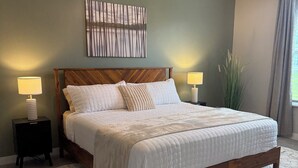 Un dormitorio con una cama de madera, dos mesitas de noche con lámparas, un tapete estampado y una obra de arte en la pared.
