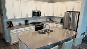 Una cocina moderna con armarios blancos, electrodomésticos de acero inoxidable, una isla central con taburetes y suelo de madera.