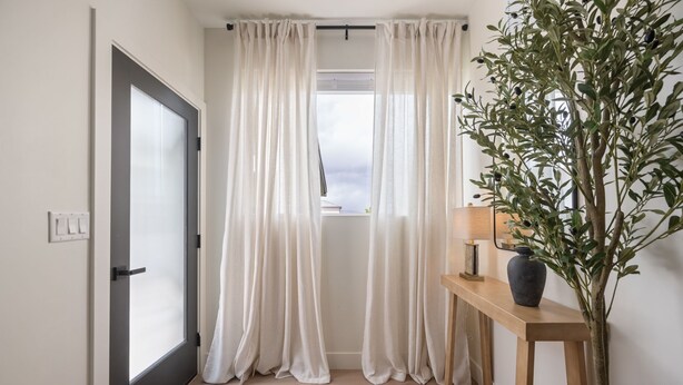 A hallway with a door, white curtains, a wooden console table with a vase, and a potted plant. - Charming 2-bedroom house Near Zion & Sand Hollow (HURRICANE)