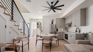 A modern kitchen with a central island, a dining area with a round table and chairs, and a staircase with black railings. - Charming 2-bedroom house Near Zion & Sand Hollow (HURRICANE)
