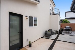A modern house with a sliding glass door, a small patio with outdoor furniture, and a brick wall. - Charming 2-bedroom house Near Zion & Sand Hollow (HURRICANE)