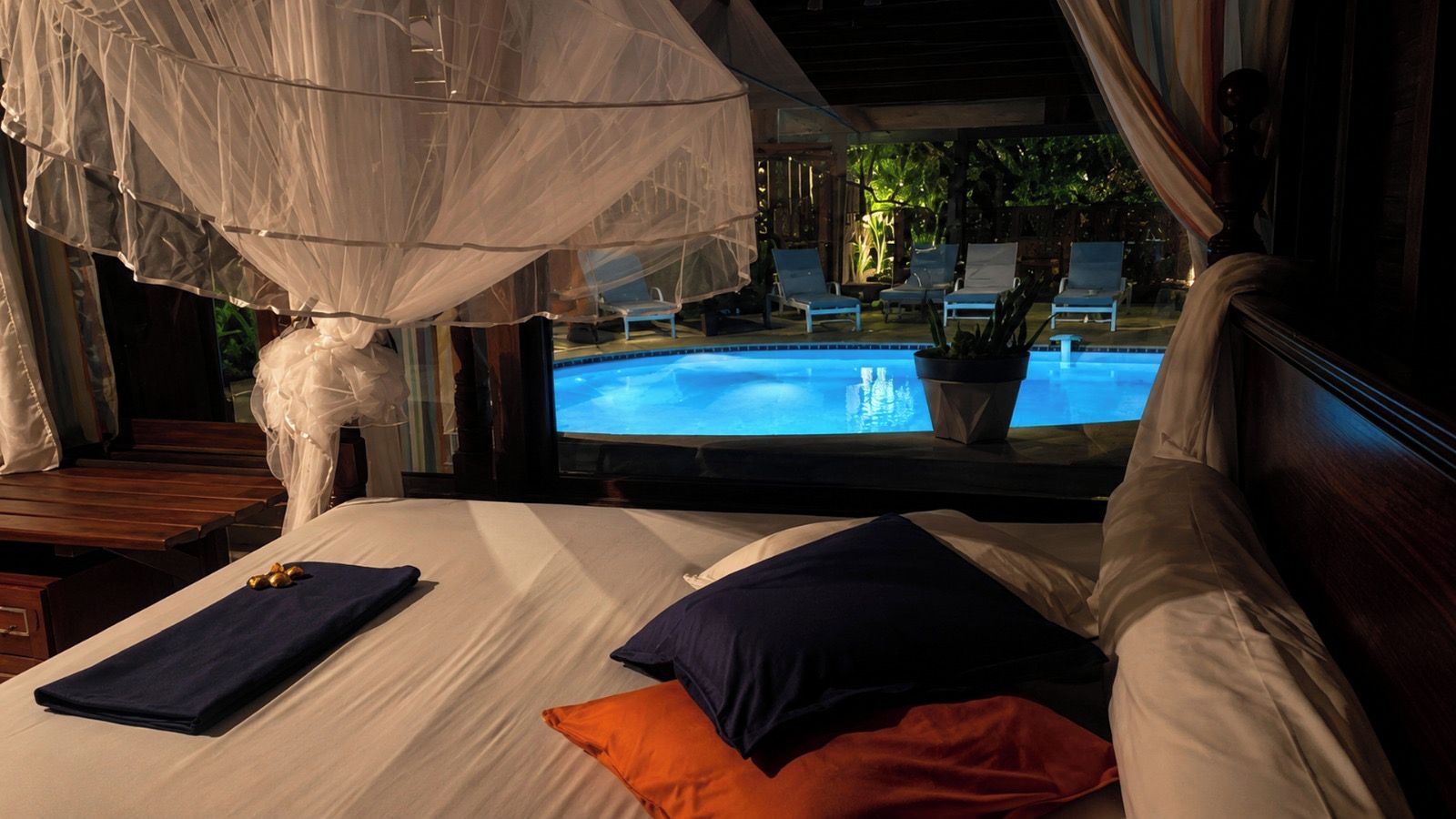 A room with a bed, a view of a pool, and a canopy.