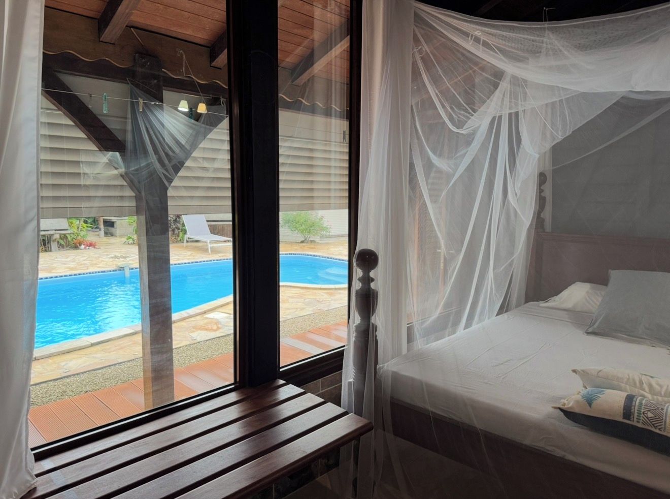 Een slaapkamer met uitzicht op een zwembad, een houten bankje en een bed met hemelbed.