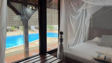 Een slaapkamer met uitzicht op een zwembad, een houten bankje en een bed met hemelbed.