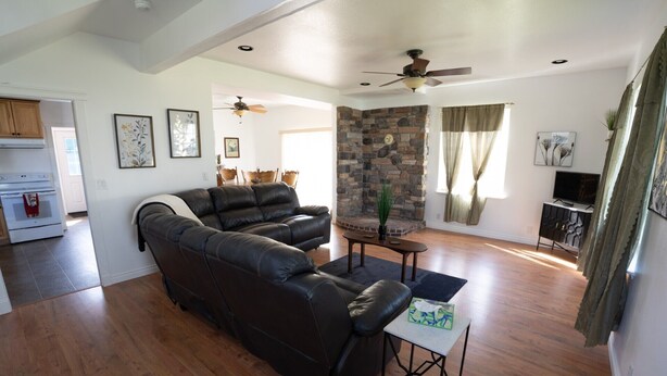 A living room with a leather sofa, a stone fireplace, a ceiling fan, and a dining area with wooden furniture.