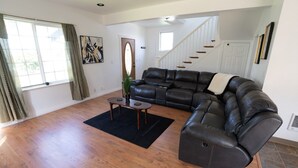 A spacious living room with a leather sofa, a coffee table, and a staircase leading to another level.