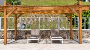 A covered outdoor seating area with two cushioned chairs and a wooden pergola structure.