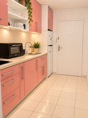 A kitchen with pink cabinets, a white refrigerator, a black microwave, and a sink with a faucet.