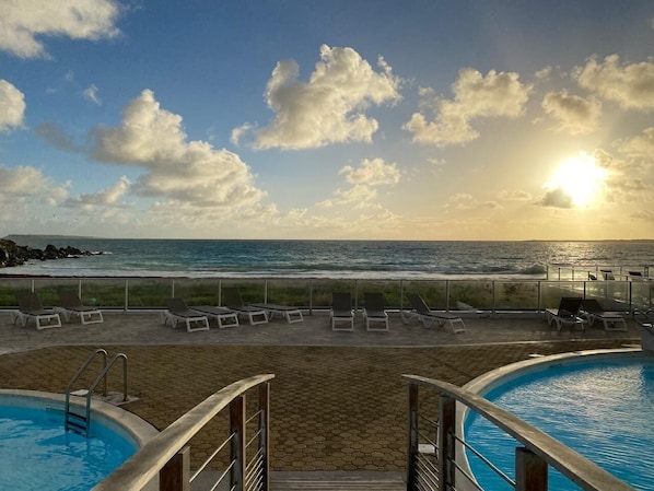 A pool area with lounge chairs and a view of the ocean at sunset.