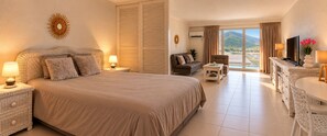 A hotel room with a large bed, a sofa, a TV, and a balcony with a view of the mountains.