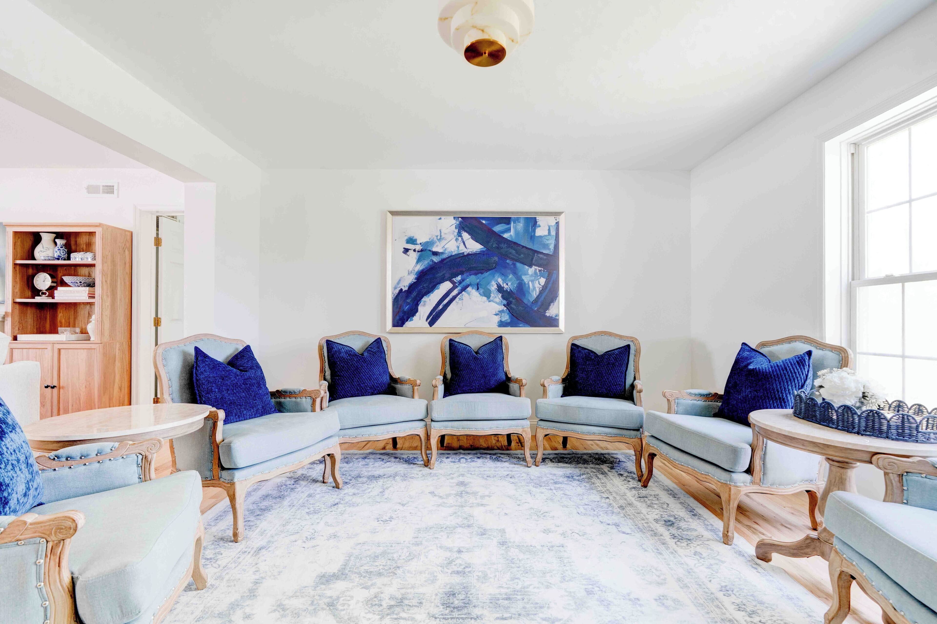 A spacious living room with a large abstract painting, a wooden cabinet, and a blue rug.