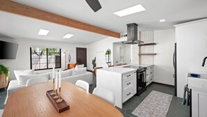 Une cuisine moderne avec des meubles blancs, un îlot central et un coin repas comprenant une table en bois et des chaises blanches.