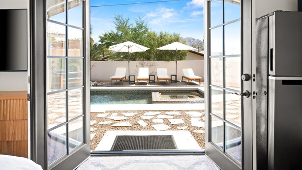 Une chambre d’hôtel moderne dotée d’une porte-fenêtre coulissante donnant sur un espace piscine aménagé avec des chaises longues et des parasols.