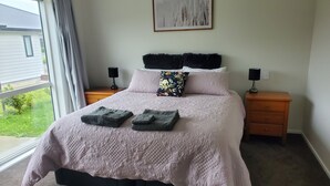 A neatly made bed with a floral pillow, two bedside lamps, and a view of the outdoors through a large window.