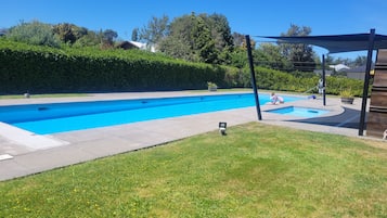 A swimming pool with a surrounding grassy area and a pergola structure.
