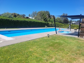 A swimming pool with a surrounding grassy area and a pergola structure.