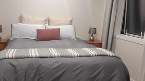 A neatly made bed with a grey and white striped blanket, two bedside tables with lamps, and a window with curtains.