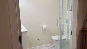 A bathroom with a glass shower enclosure, a toilet, and a marble floor.