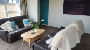 A living room with a black leather sofa, a wooden coffee table, and a white blanket draped over a black leather chair.