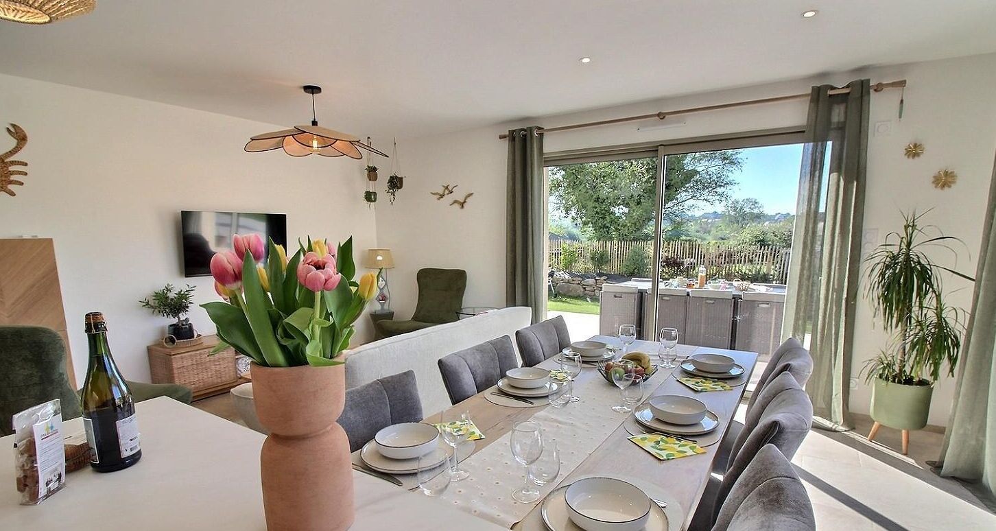 Comedor con mesa dispuesta para seis personas, un ventanal con vistas al exterior y un florero con flores sobre la mesa.