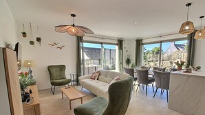 Una sala moderna con un sofá, sillas, un comedor y ventanas amplias que ofrecen vistas al exterior.