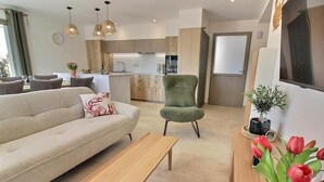Una sala de estar moderna con un sofá, un sillón verde, una mesa de centro de madera y un televisor montado en la pared.