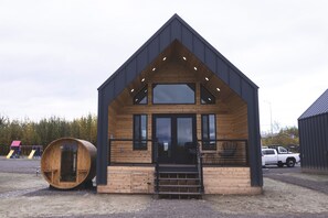 A modern wooden cabin with a steep gabled roof, large windows, and a wooden barrel-shaped structure nearby. - Lakefront Cottage with Sauna- #2 Coho (Wasilla)