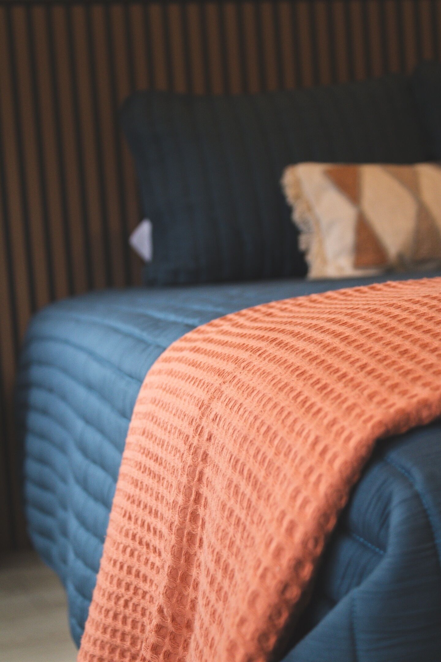 A bed with a blue quilt and an orange blanket.