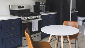 A modern kitchen with dark blue cabinets, a stainless steel stove, and a white dining table with two chairs. - Lakefront Cottage with Sauna- #2 Coho (Wasilla)