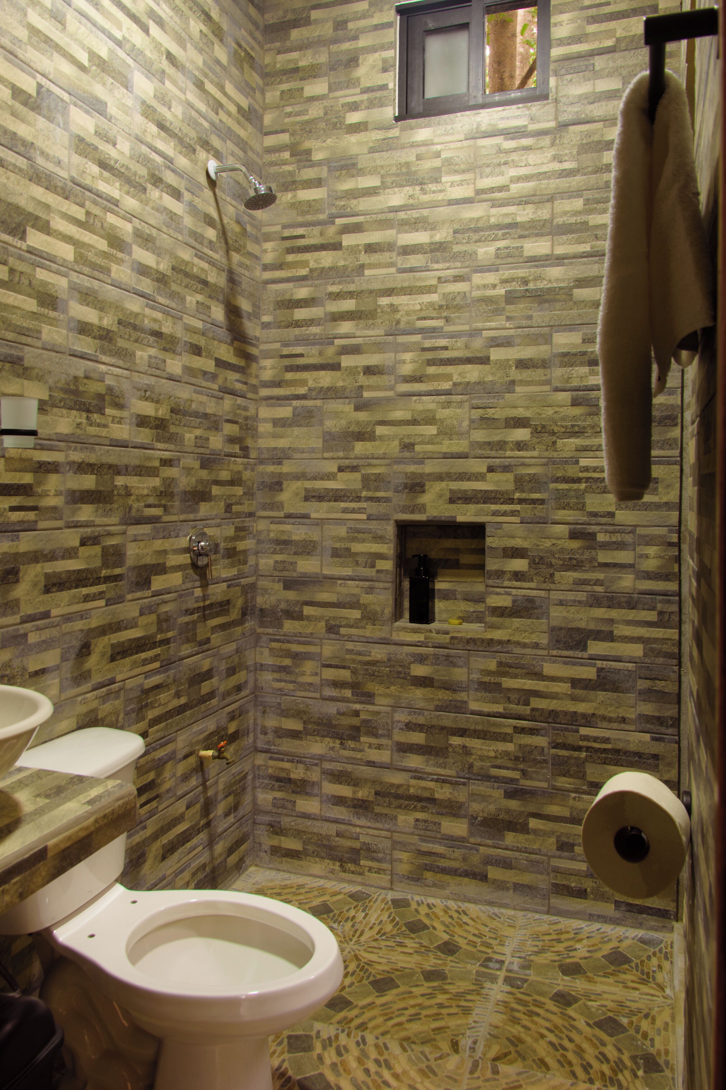 Ein Badezimmer mit gefliesten Duschwänden, einer Toilette und einem Handtuchhalter.