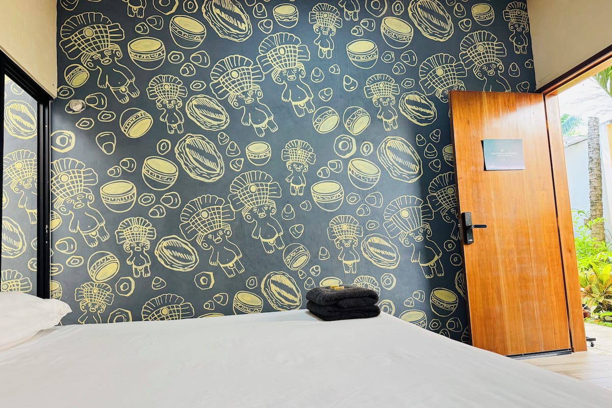 A hotel room with a bed, a wooden door, and a wall with a patterned design.