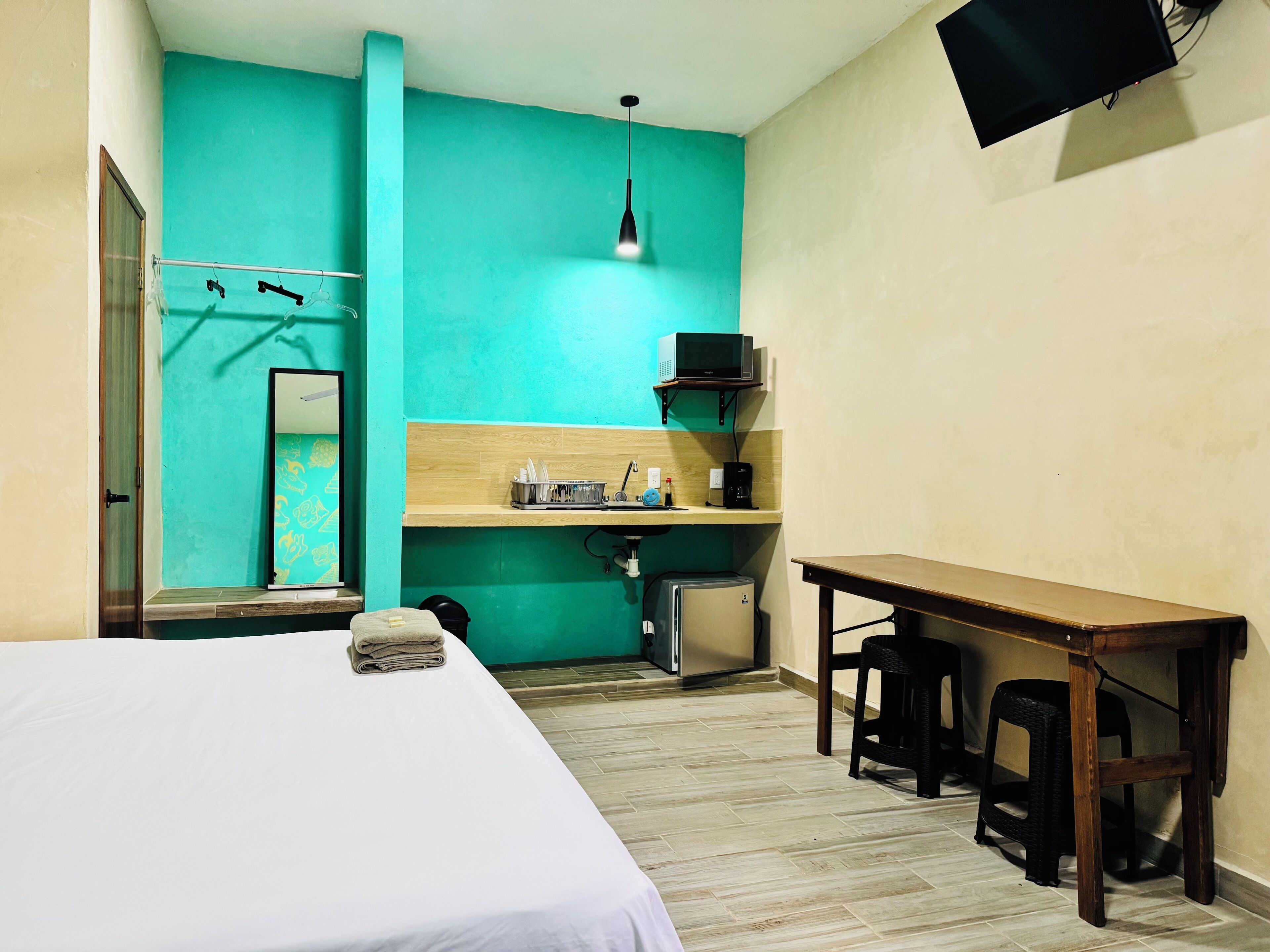 Ein Hotelzimmer mit einem Bett, einem Schreibtisch, einer Mikrowelle, einem Kühlschrank und einem an der Wand befestigten Fernseher.