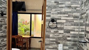 A bathroom with a stone-patterned wall, a wooden door, a sink, and a window with a view of greenery. - Ceremonial Tulum (Tulum)