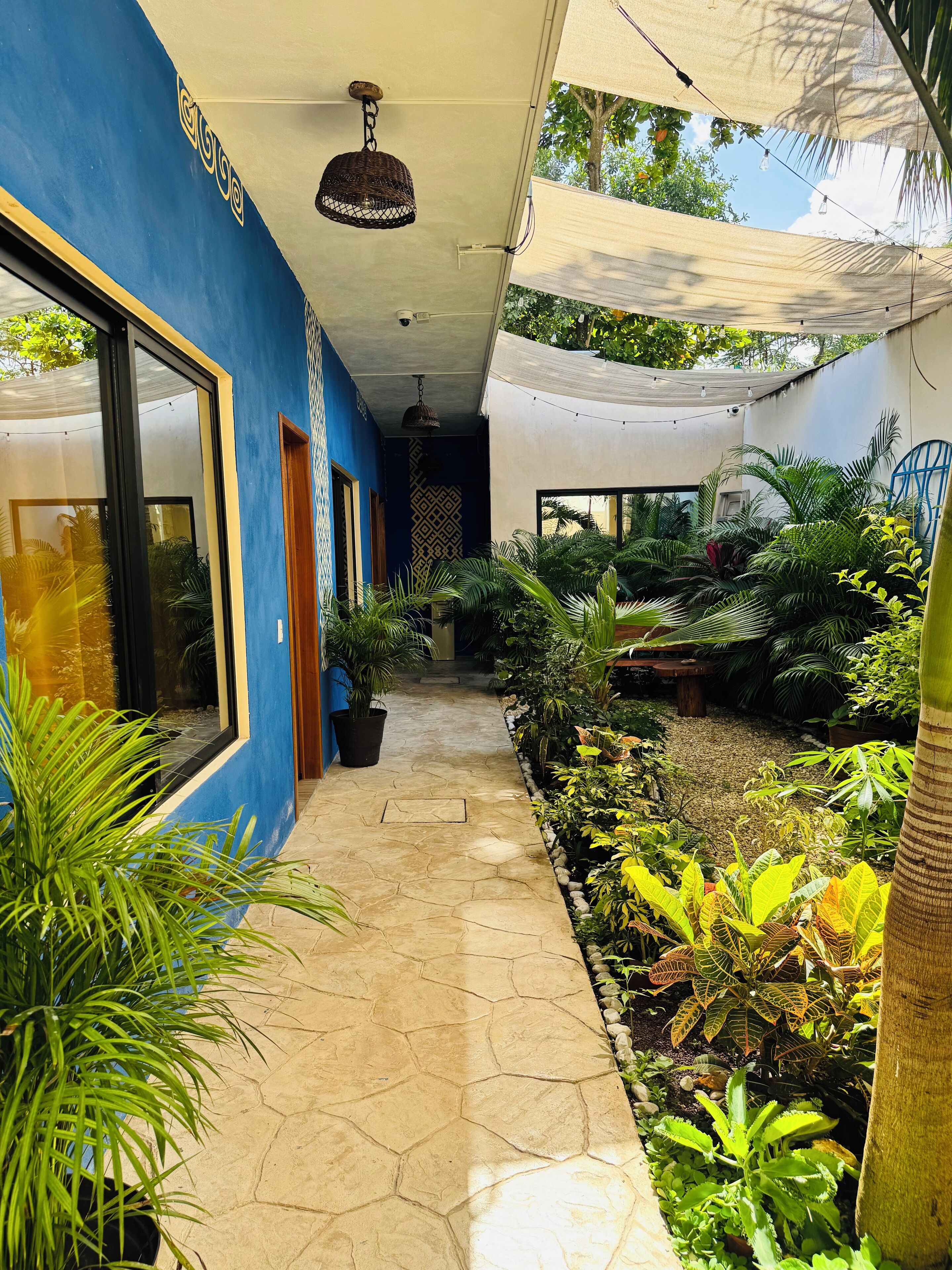 A covered walkway with a tiled floor, surrounded by lush greenery and potted plants.