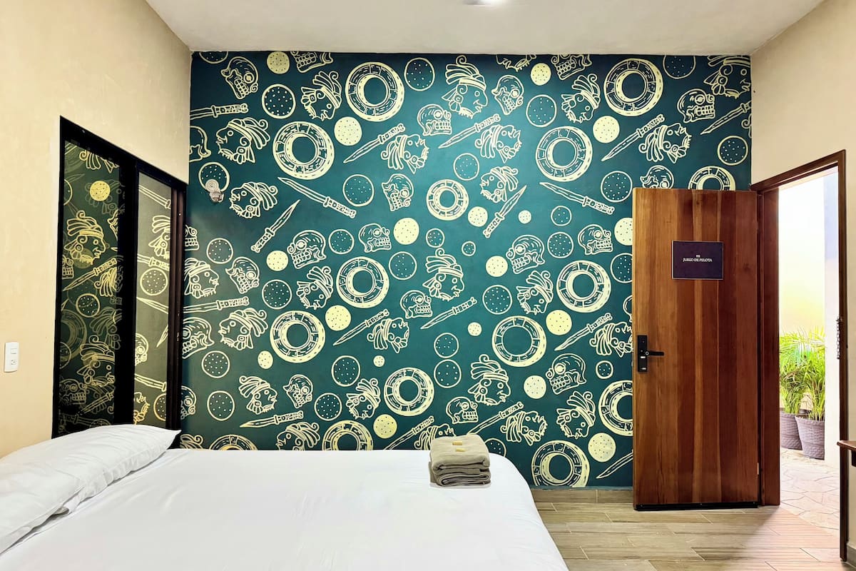 A hotel room with a bed, a wooden door, and a wall with a decorative pattern.