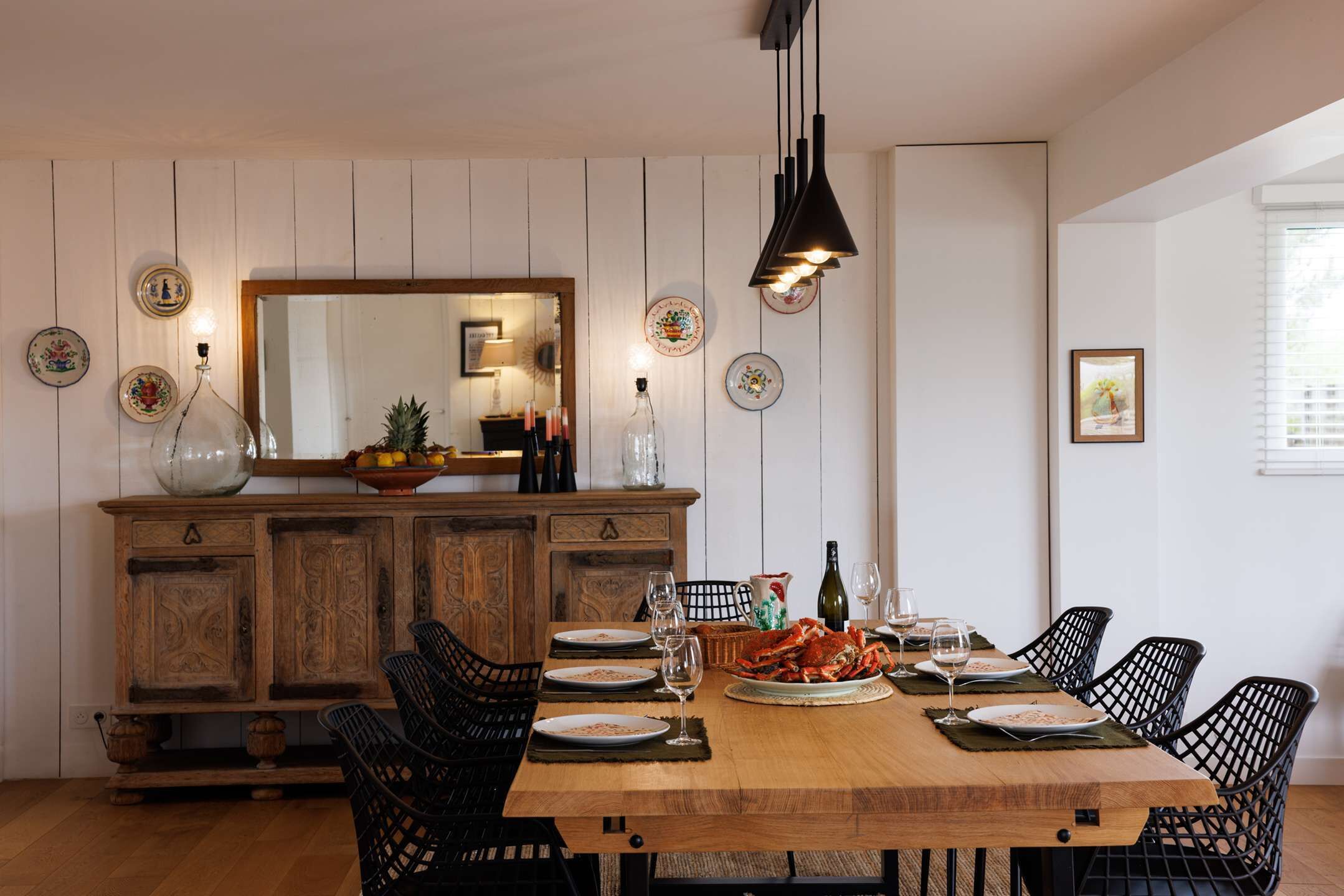 A dining area with a wooden table, black chairs, and a large mirror above.
