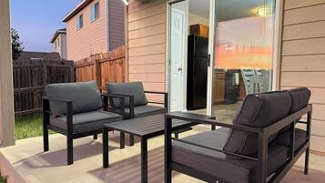 Un patio al aire libre con una mesa y dos sofás, una valla de madera y un ventanal corredero que da a una cocina.