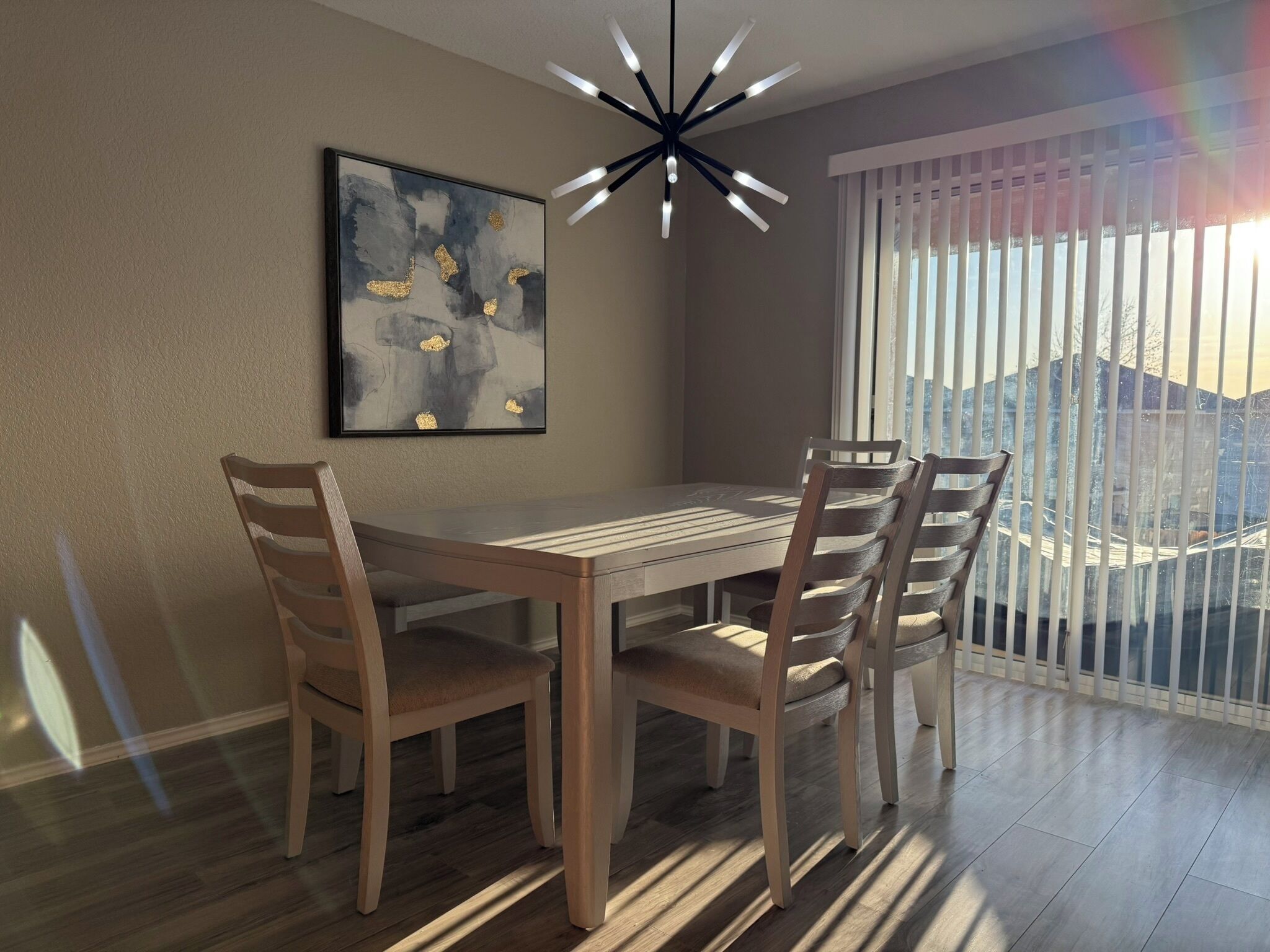 Un comedor con mesa y sillas de madera, una lámpara moderna y un amplio ventanal con persianas.