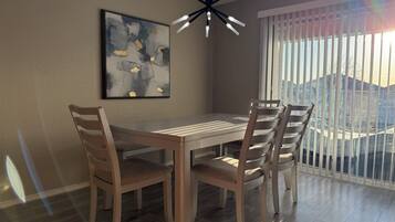 Un comedor con mesa y sillas de madera, una lámpara moderna y un amplio ventanal con persianas.