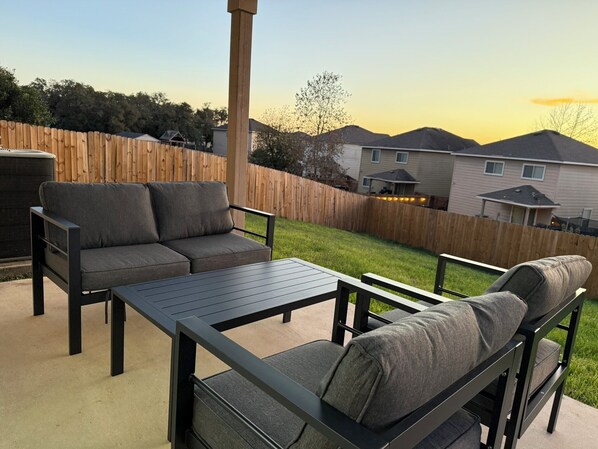 An outdoor patio with a sofa and table, surrounded by a wooden fence and houses in the background.