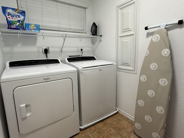 A laundry room with two white Whirlpool washers, a shelf with laundry detergent, and a towel rack.
